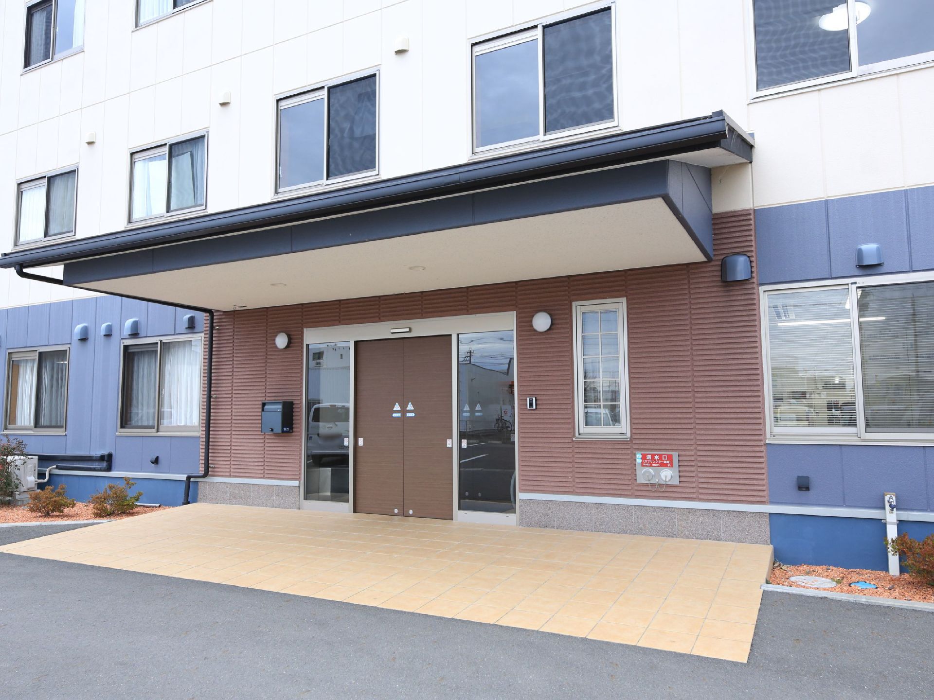 外から見た正面玄関口。自動ドアの上にはひさしが取りつけてある。左右のスペースには植え込みが設けられている。