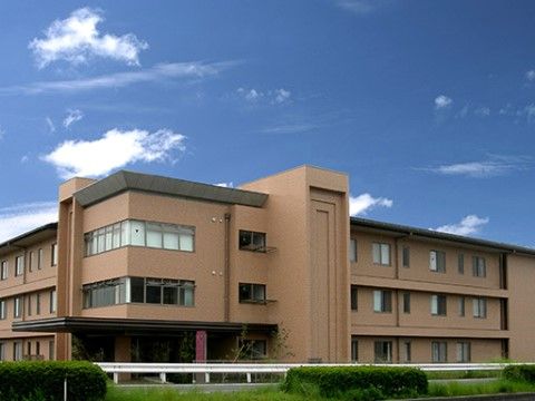 茶色い壁面の3階建てになっている。建物のまわりにはガードレールが設置され、道を挟んだところには植え込みがある。