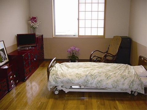 フローリングの部屋には電動ベッドや木製のチェア、高級感のあるタンスなどが置かれている。窓には障子が付いている。