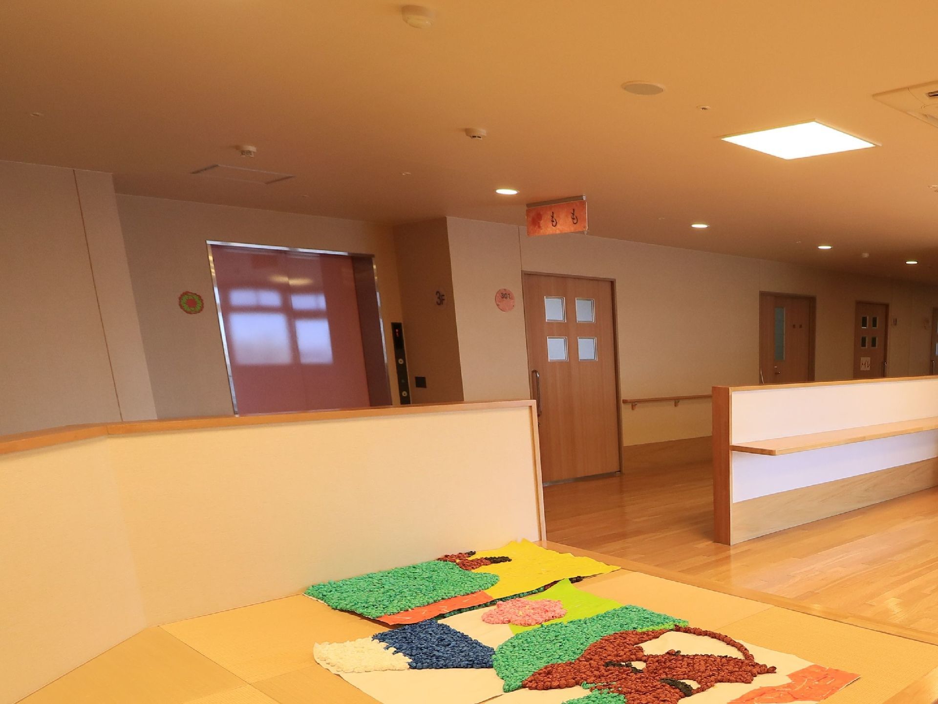 木目を基調とした空間に畳が敷かれたコーナーがある。ピンク色の扉のエレベーターの前にももと書かれた看板が設置されている。
