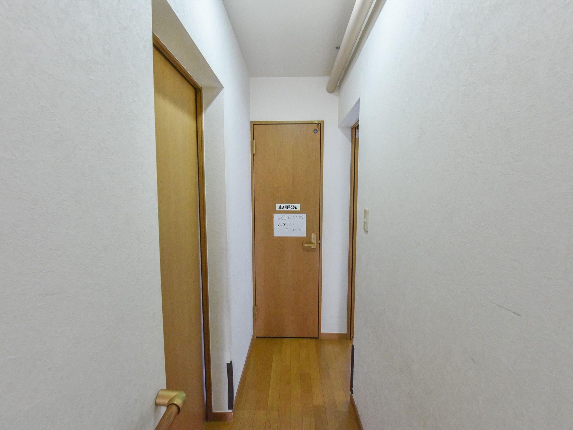 通路には手すりを設置している。トイレが通路の奥にある。入居者様への注意喚起がトイレのドアに貼られている。