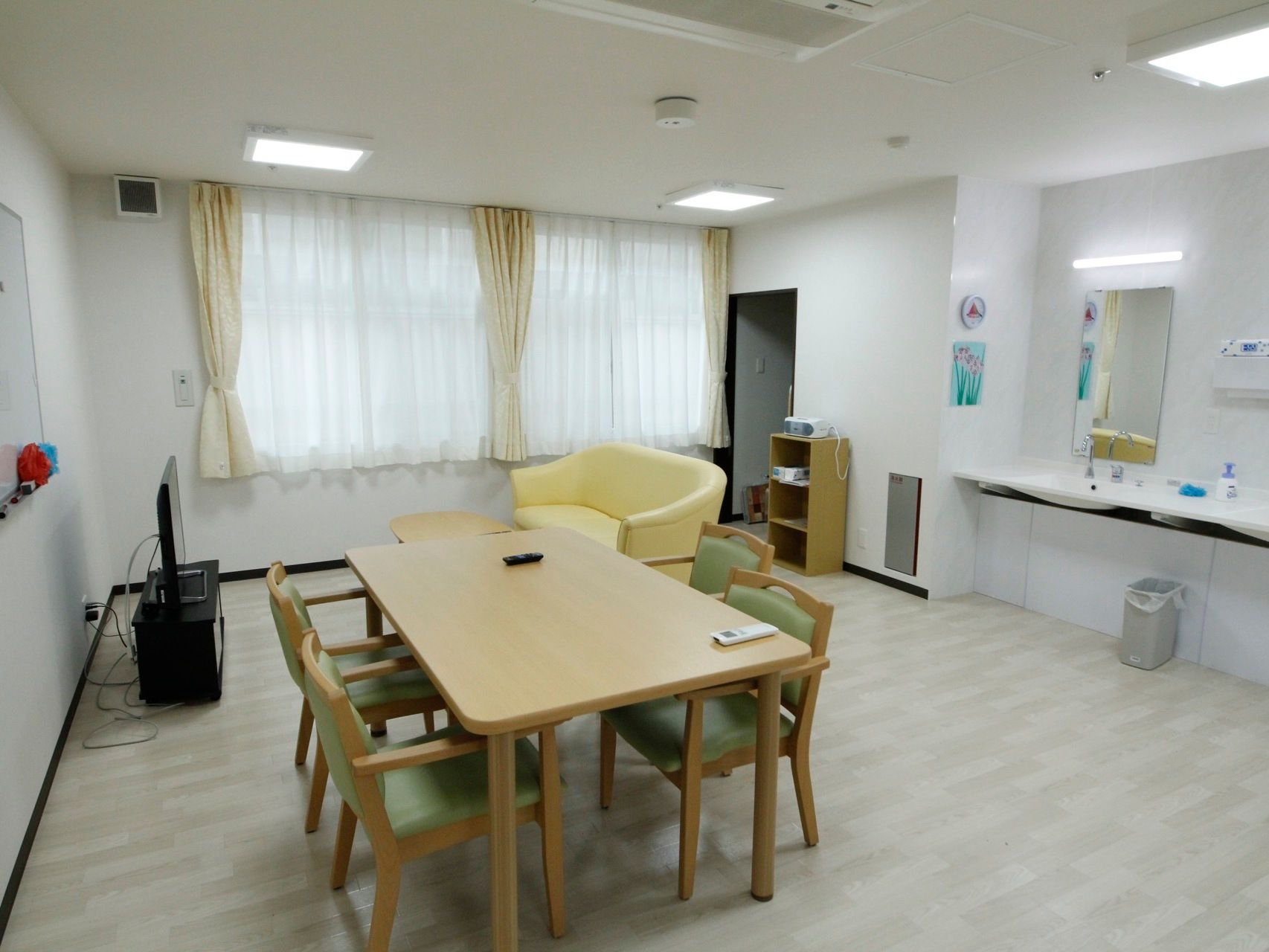 食堂には、洗面スペースが備わっている。４人掛けダイニングテーブルやテレビが配置されており、壁にホワイトボードが掛けられている。