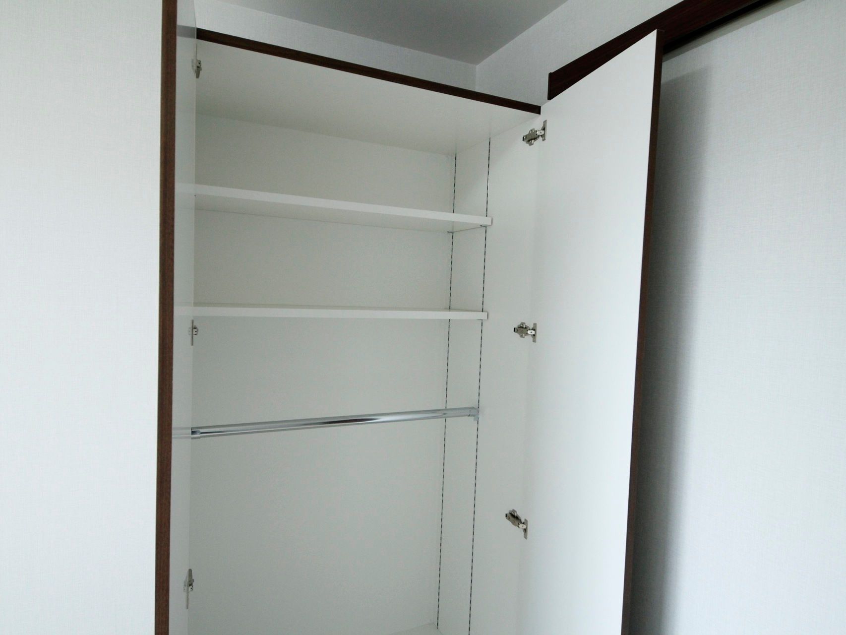 扉が両開きの収納家具が居室の一角に置かれている。中は白く２段式棚の下にハンガーポールが取り付けられている。