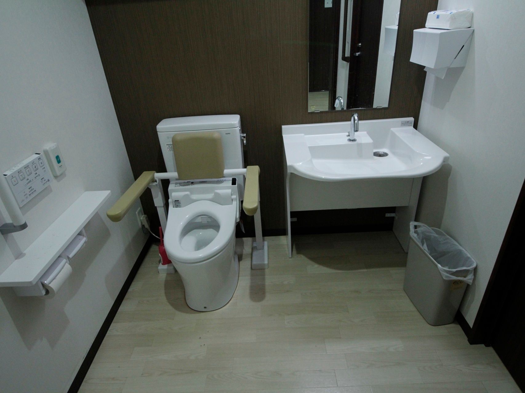 車椅子や介助者が入れる広いトイレである。便器の横に洗面台が設置されている。温水洗浄便座のリモコンが壁に取り付けられている。