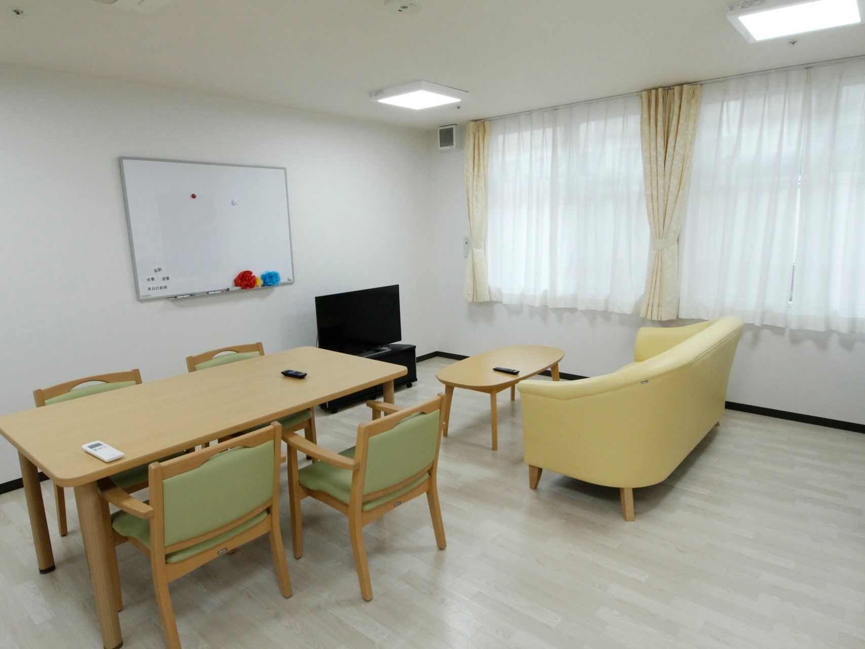 ホワイトボードが壁に取り付けられ、テレビとソファーが設置された食堂
