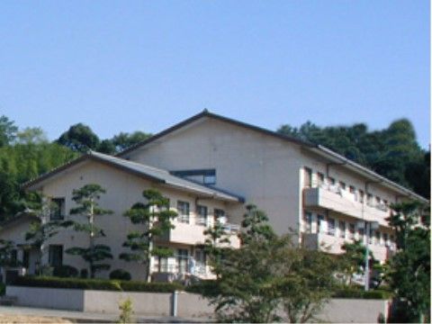 緑に囲まれ大きな松が周りに植えられた三角屋根の施設