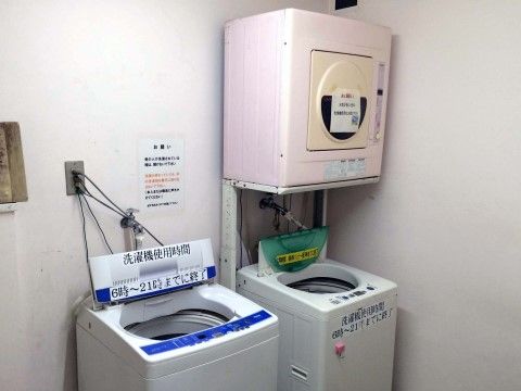 縦型洗濯機が２台、乾燥機が１台用意されている。洗濯機の使用時間について、6時〜21時という貼り紙がある。