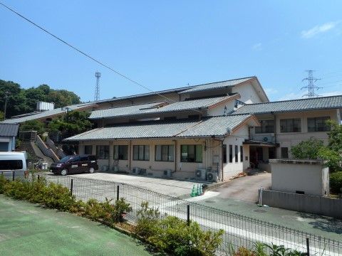 フェンスに囲まれた広い敷地があり、窓の並ぶ瓦屋根の建物