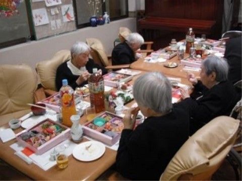 長テーブルでソファーに座りながらお弁当を食べる入居者たち