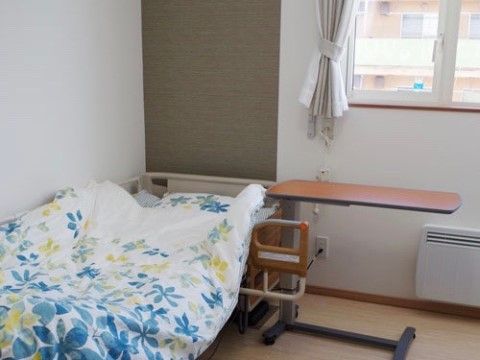 花柄の布団が被せられ、小さなテーブルの付いた窓際にあるベッド