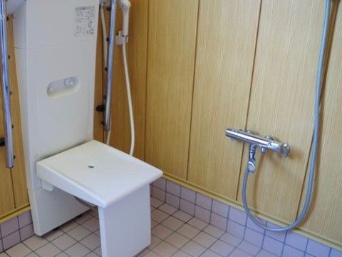 浴室の隅には、背もたれの高い白を基調とした折り畳み椅子が設置されている。その横の壁にシャワーが取り付けられている。