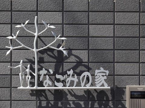グレーのタイルに掲げられた、施設名と大きな木の下で肩を組むオブジェ
