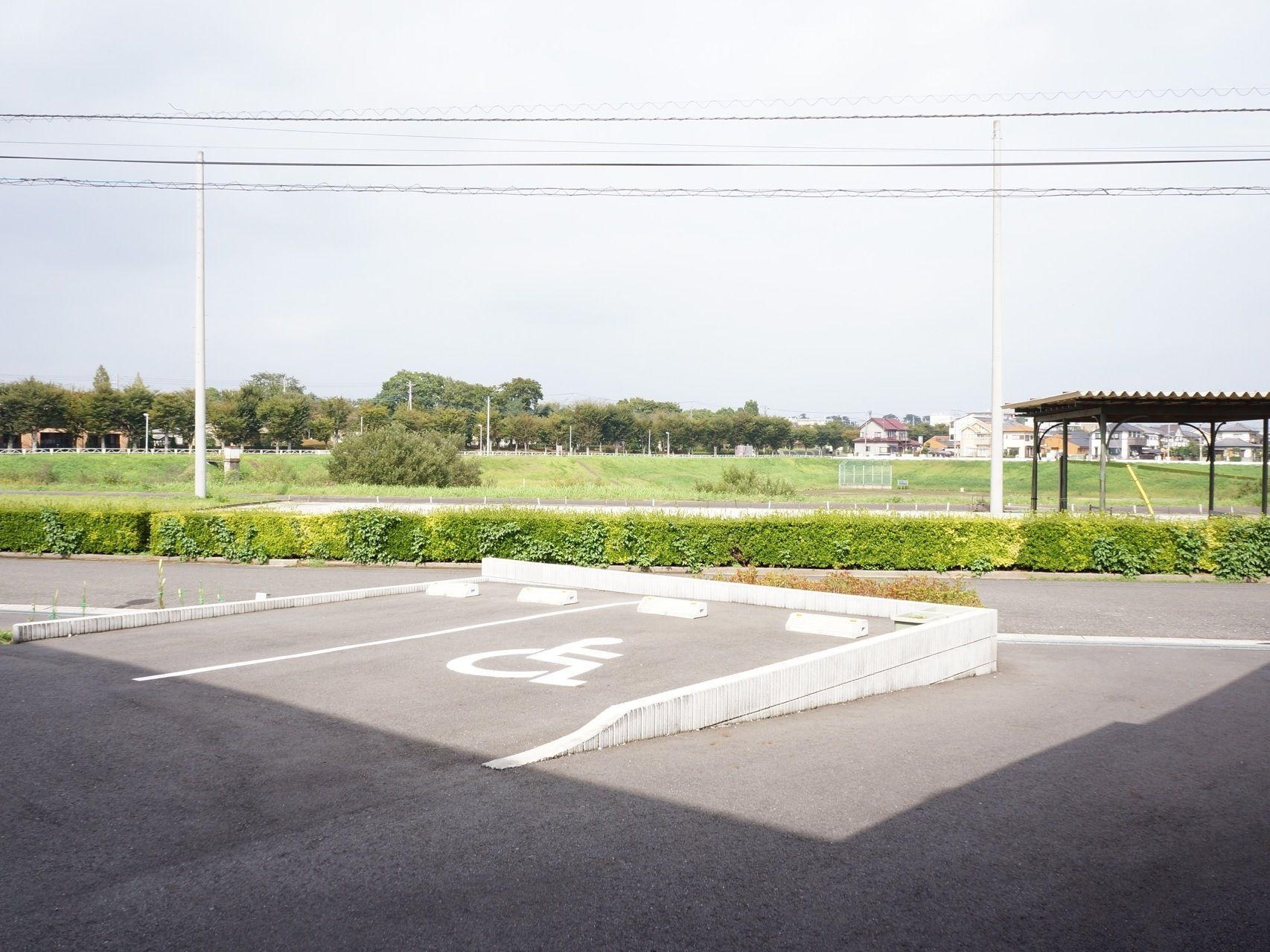 施設の駐車場には、身障者スペースも設けられている。近くに河川敷が見える。周囲には木々が植えられ、緑の多い場所である。