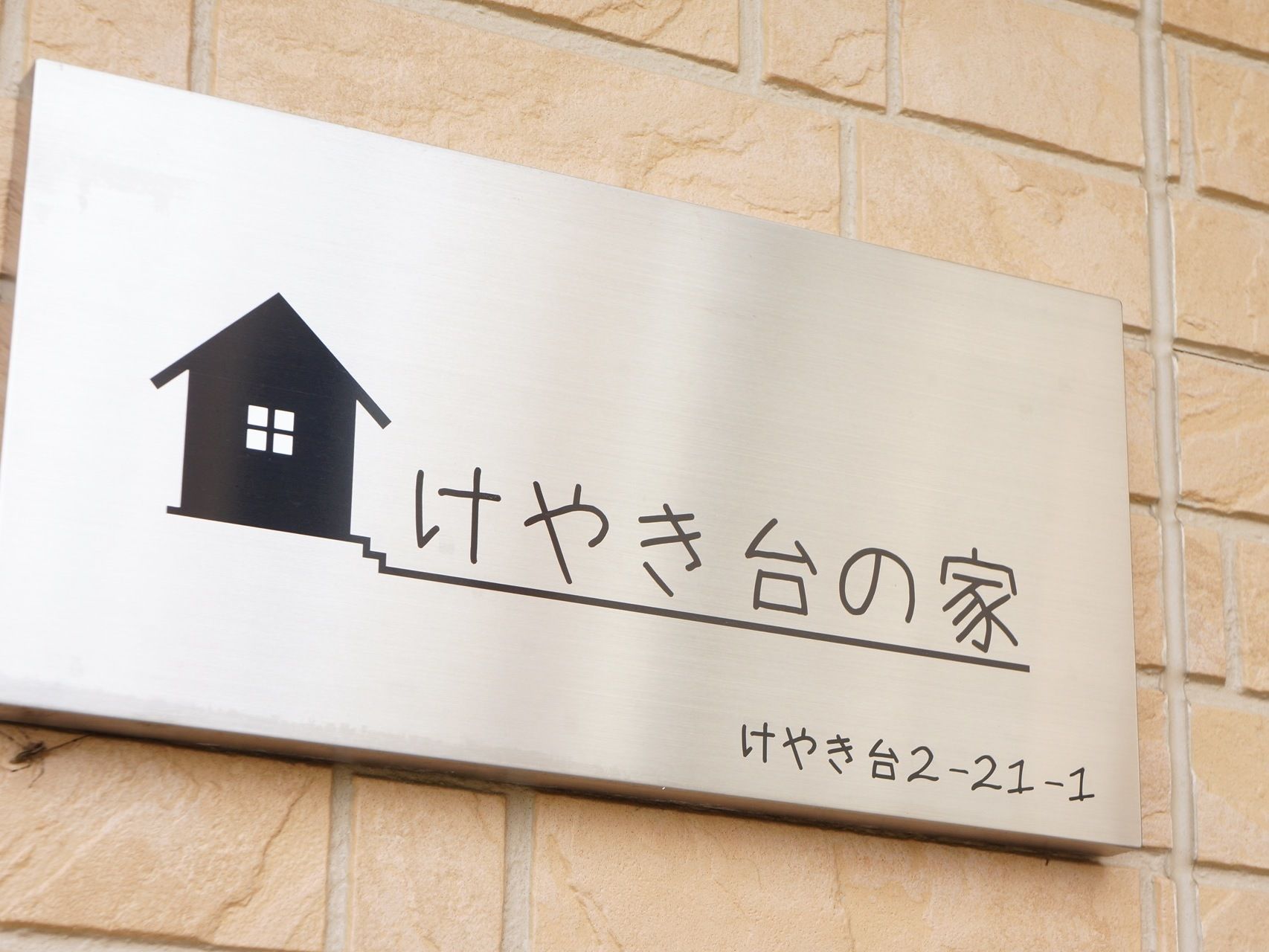 レンガ造り風の壁に、看板が付いている。看板はスチール製で、マークと施設名、施設の住所が表記されている。