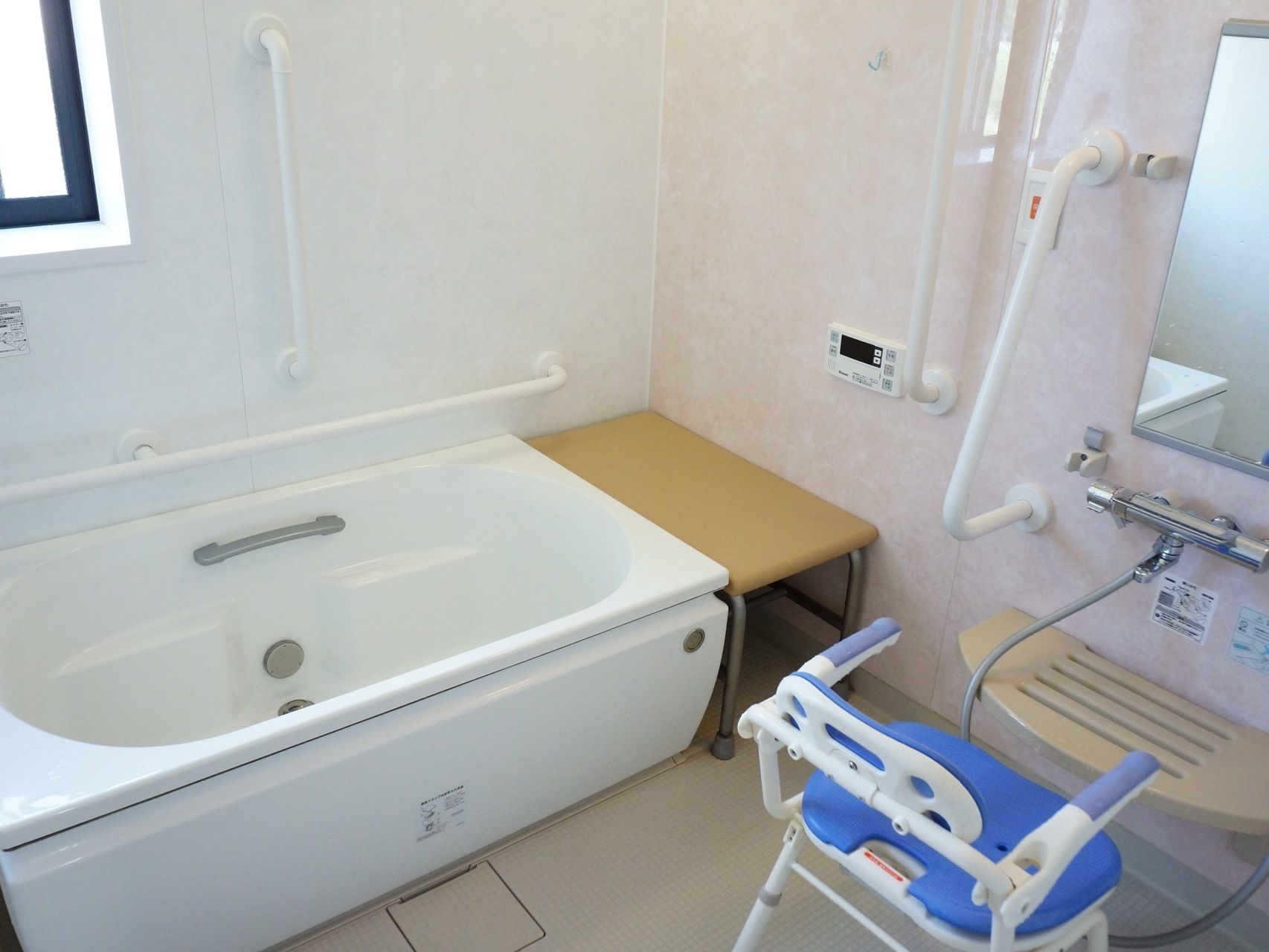 浴室内に、浴槽に加えシャワーが付いているタイプの風呂場。シャワーチェアが置いてあり、壁に手すりが付いている。