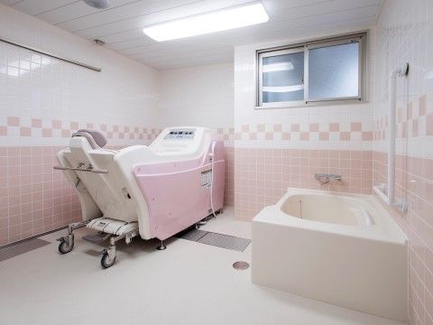 手すりが取り付けられたタイル張りの浴室内にあるユニットバスと機械浴槽