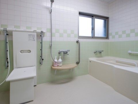 白色と淡い黄緑色のタイル張りの浴室で、換気用の窓がある。白色の浴槽が備わり、壁には手すりが取り付けられている。