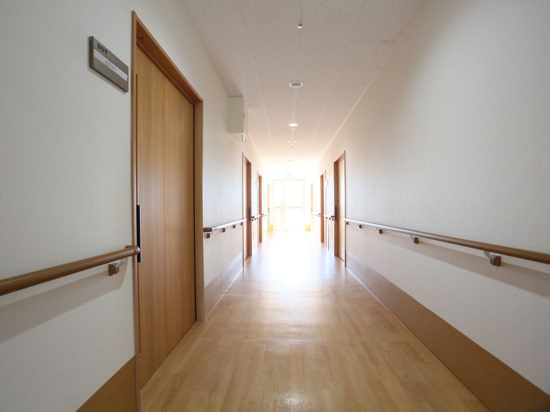 居室の扉がいくつか見えている。扉の横には部屋番号が書かれた表札がかかっている。壁には手すりが設けられている。