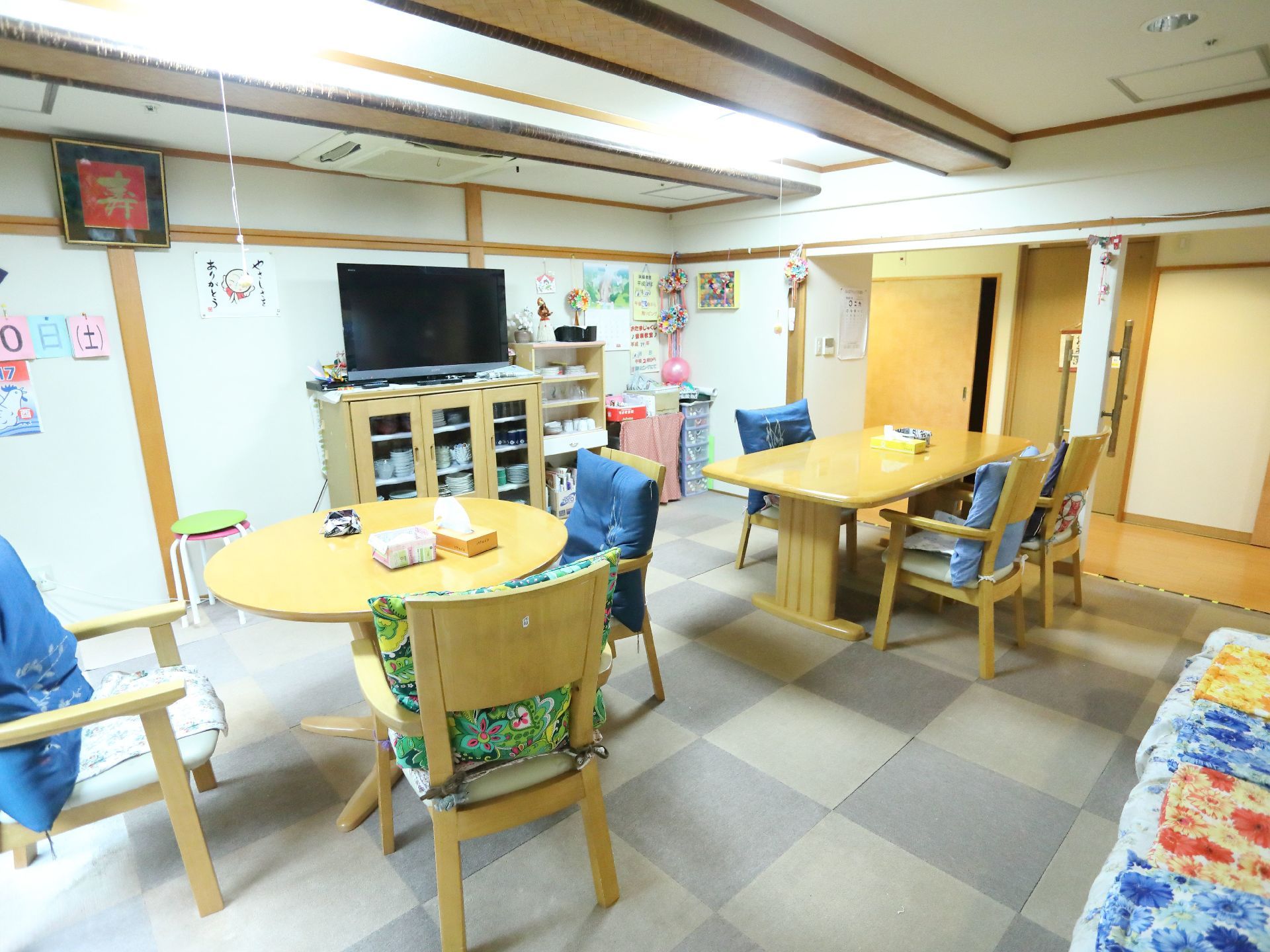 リビングには長方形と円形のテーブルがあり、周りには椅子が並べられている。食器棚の上にはテレビが置かれている。