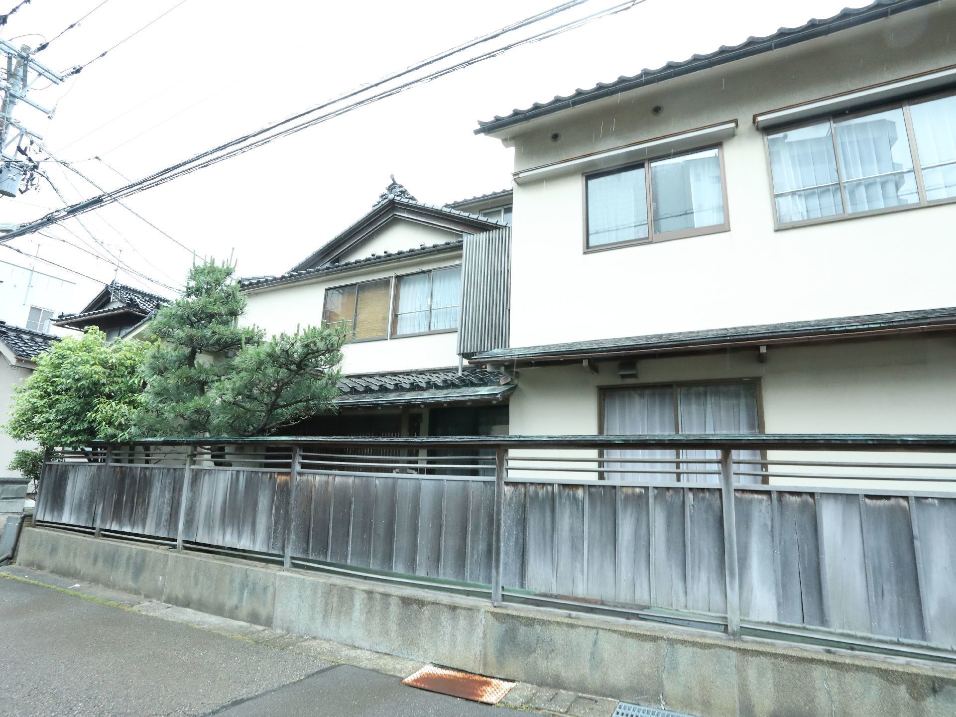 木がそばに植えられ、木材の塀で囲まれた瓦屋根の日本家屋