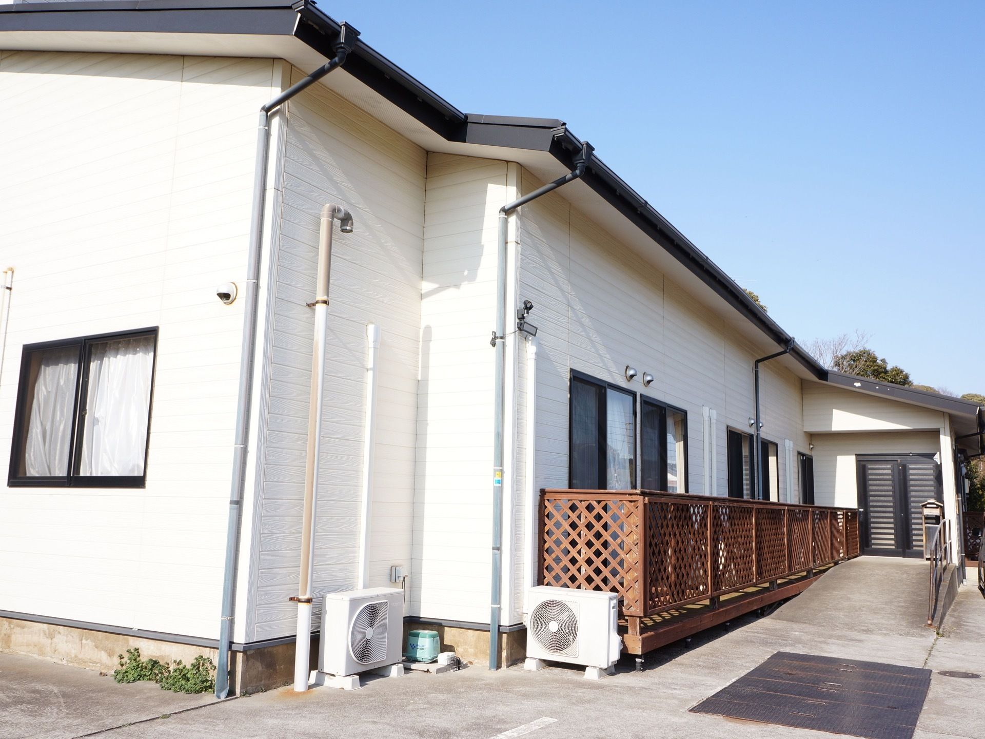 白を基調とした、一軒家のような建物。建物の周りは、段差の無いフラットな造り。玄関横には、ウッドデッキが設置されている。