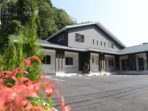 背面に大きな木々が生い茂り、広い駐車スペースのある建物