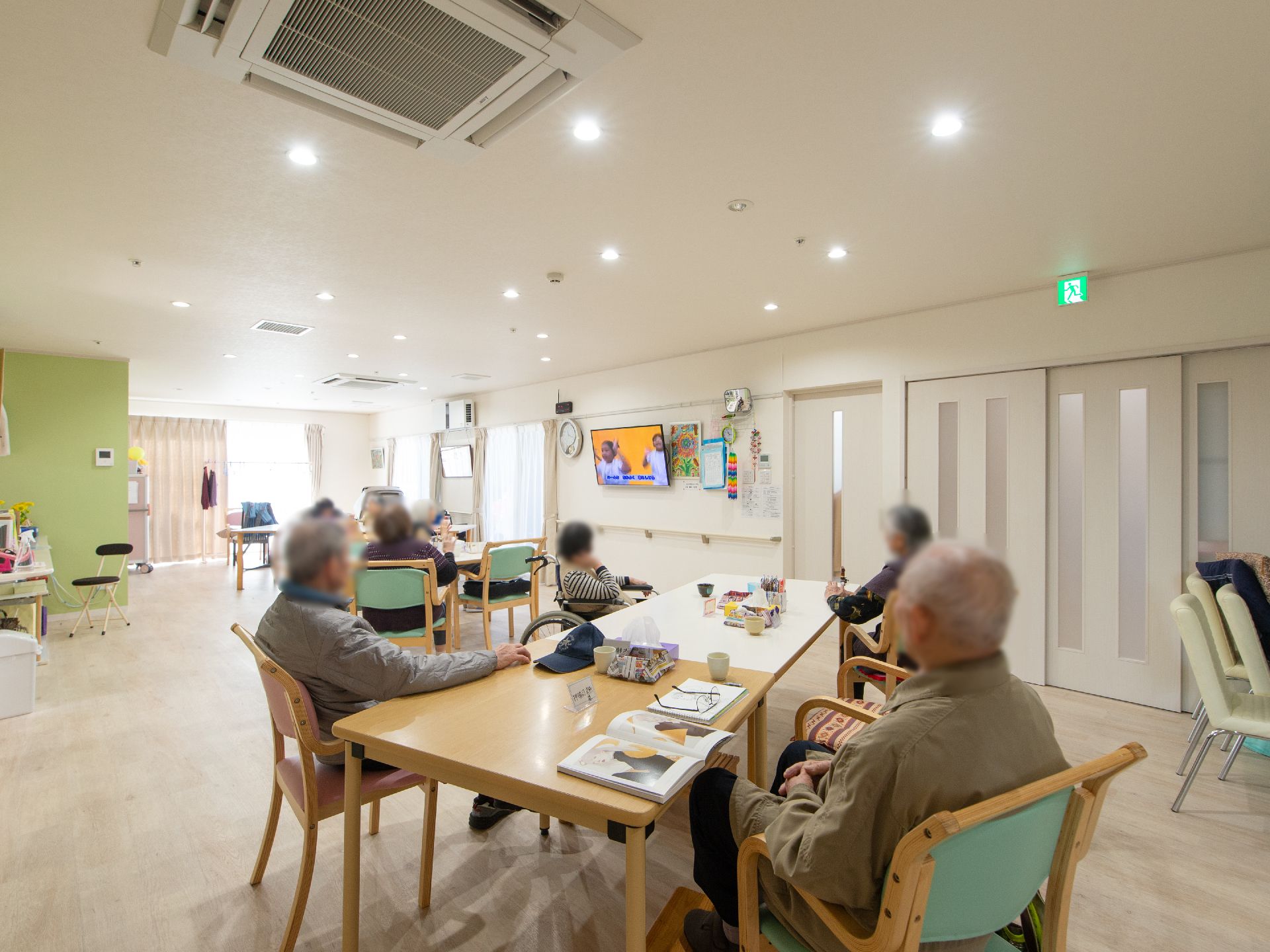 広さに余裕のあるつくりをした共有スペース。やや高い所に壁掛けテレビがあり、斜め下に角度をつけて取りつけられている。
