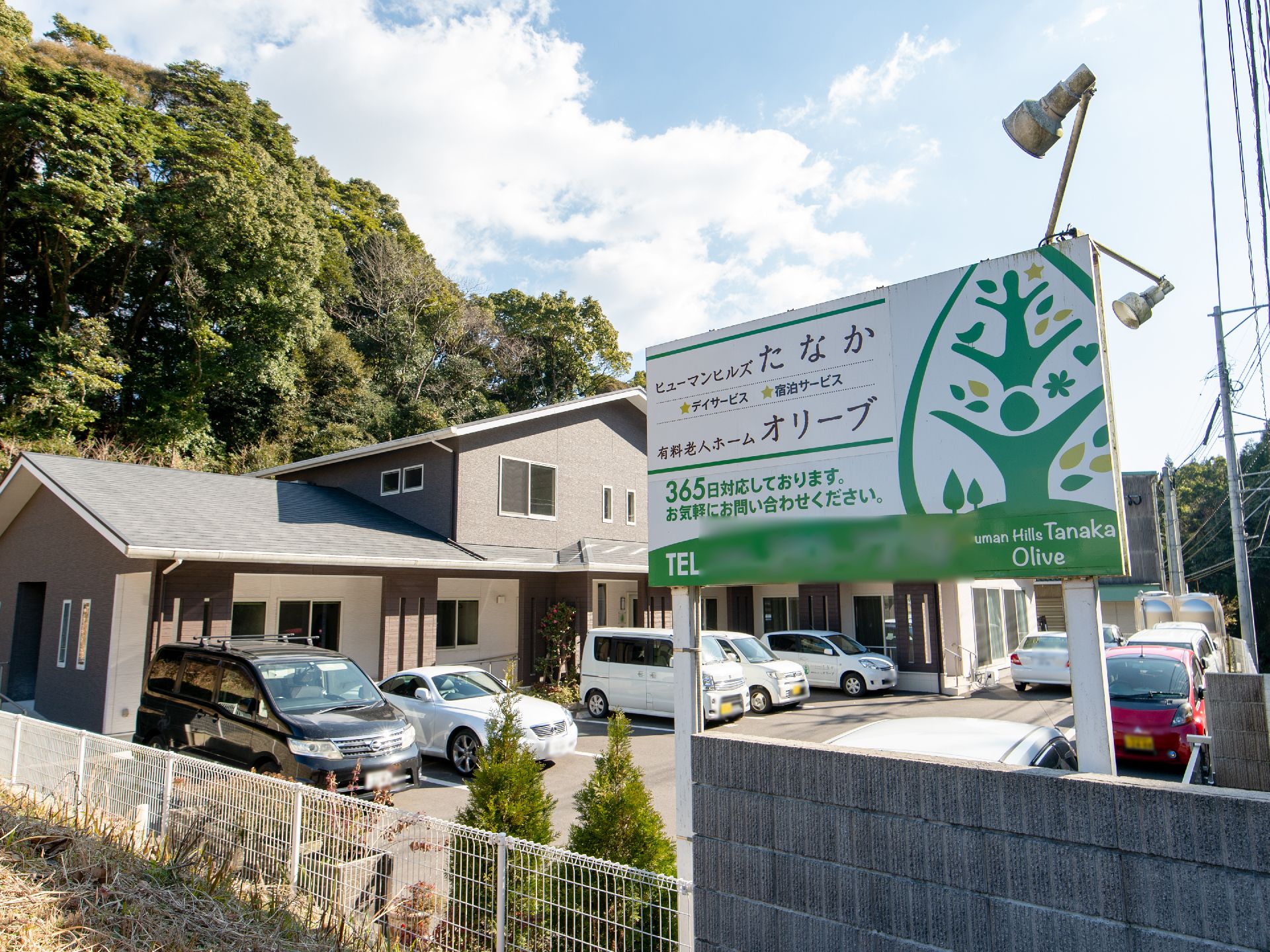 道路から見える方向に向け、施設の看板が立てられている。人と木をデザインした図案のイラストが描かれている。