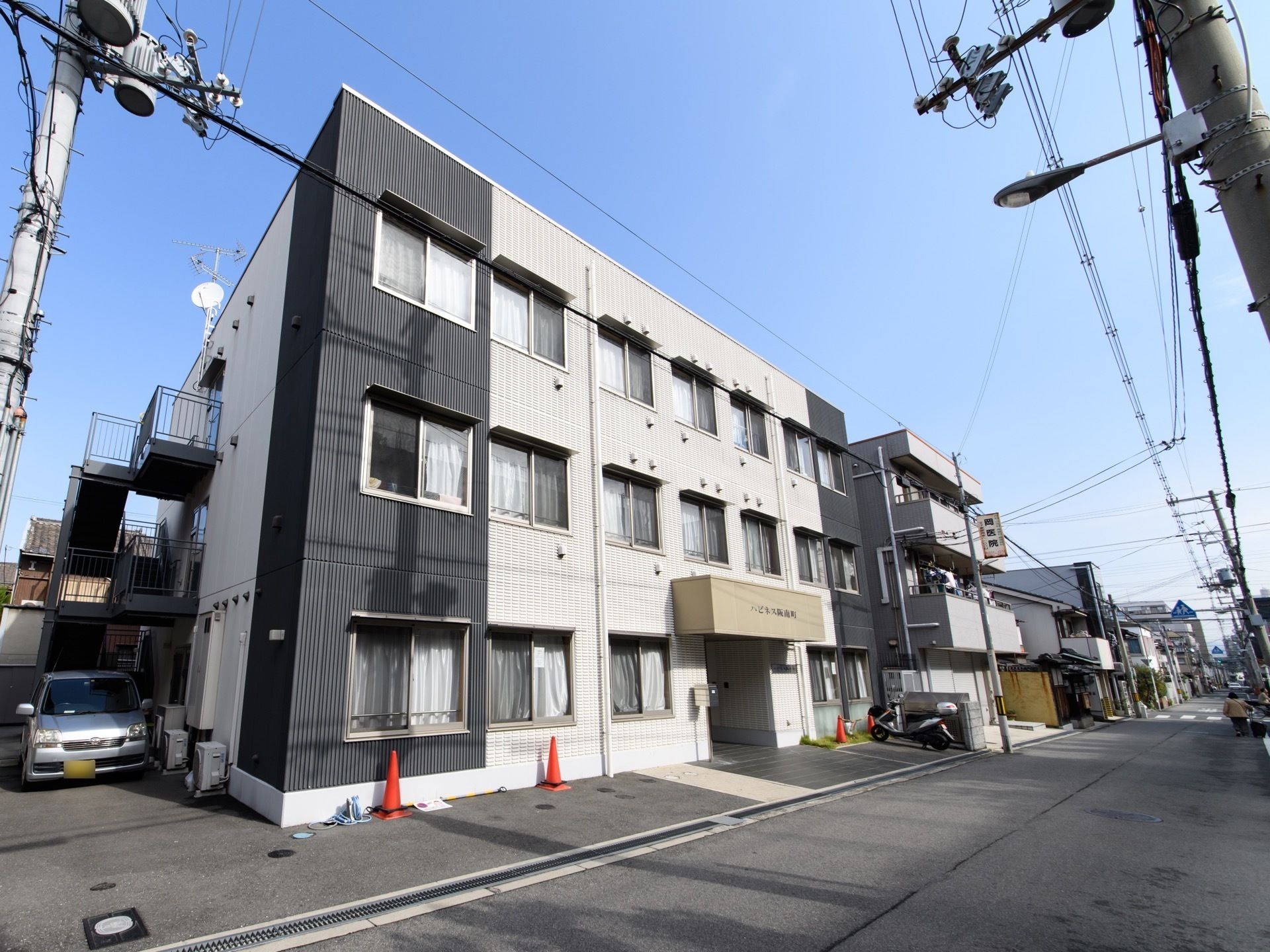 外観はシックで落ち着いたており、外壁は黒と白のパネルで覆われている。前の道は広いので車も人も利用しやすい。