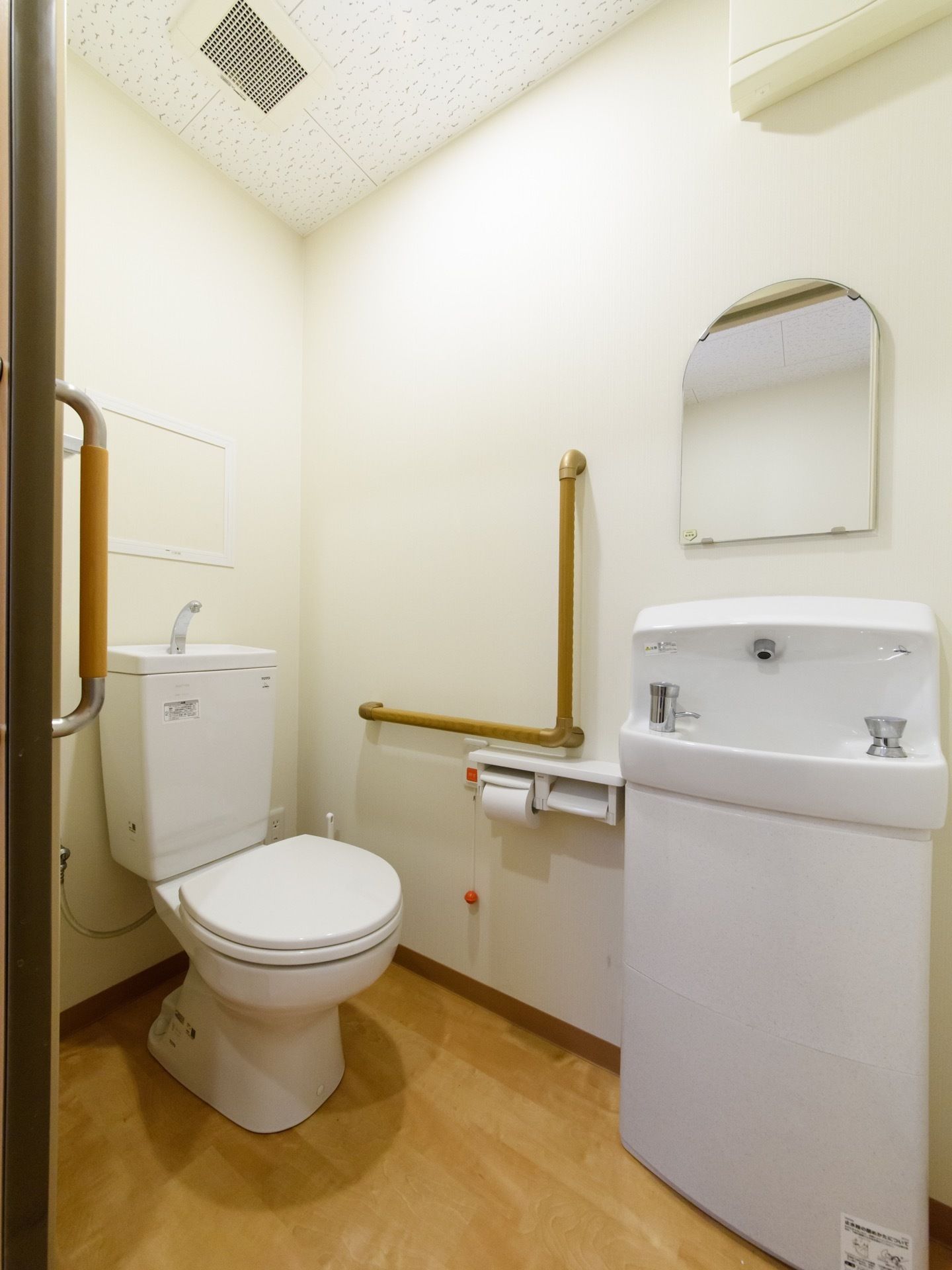 広々とした白い壁のトイレは綺麗で清潔感がある。洗面台、緊急呼出ボタン、手すりが設置されているので快適に利用できる。