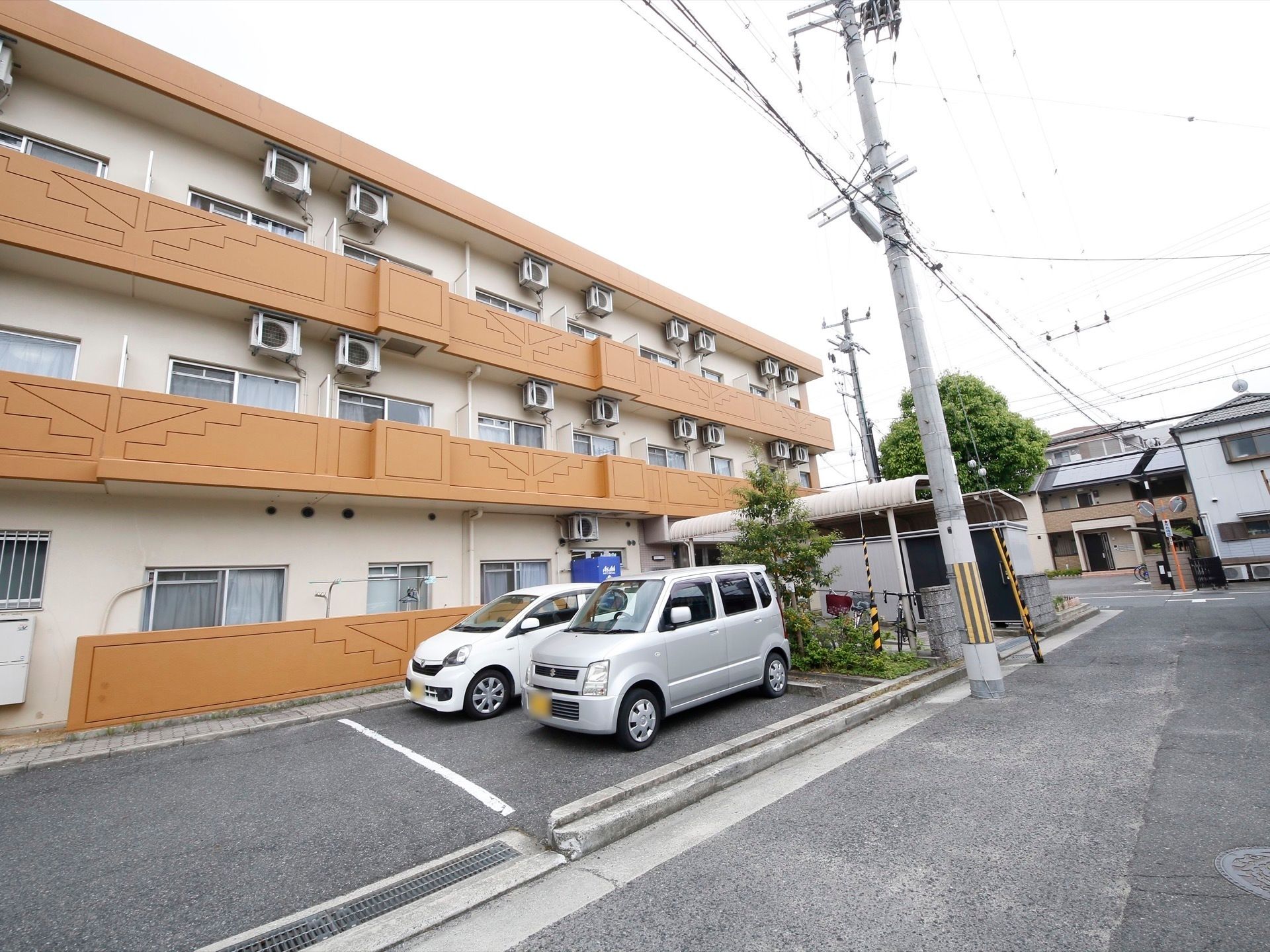 茶色いベランダが印象的で、アパートと変わらない作りに見える。駐車場と駐輪場があり、自動車などが何台かとまっている。