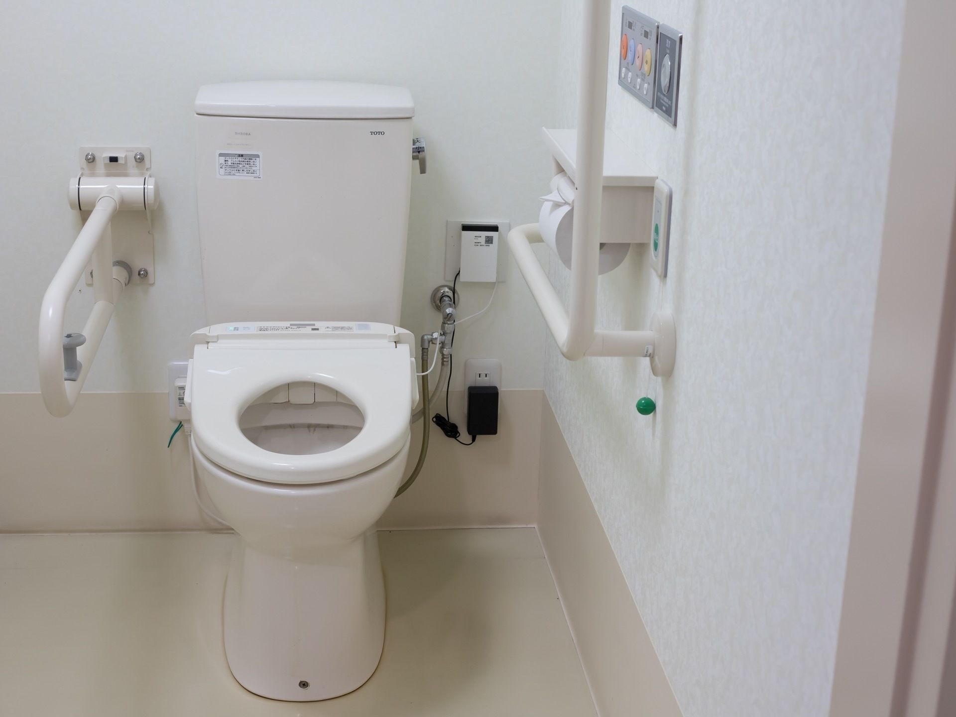 壁には水洗のスイッチのほかにも、お尻を洗う機能のスイッチがついている。便座の横には、可動式の手すりがある。