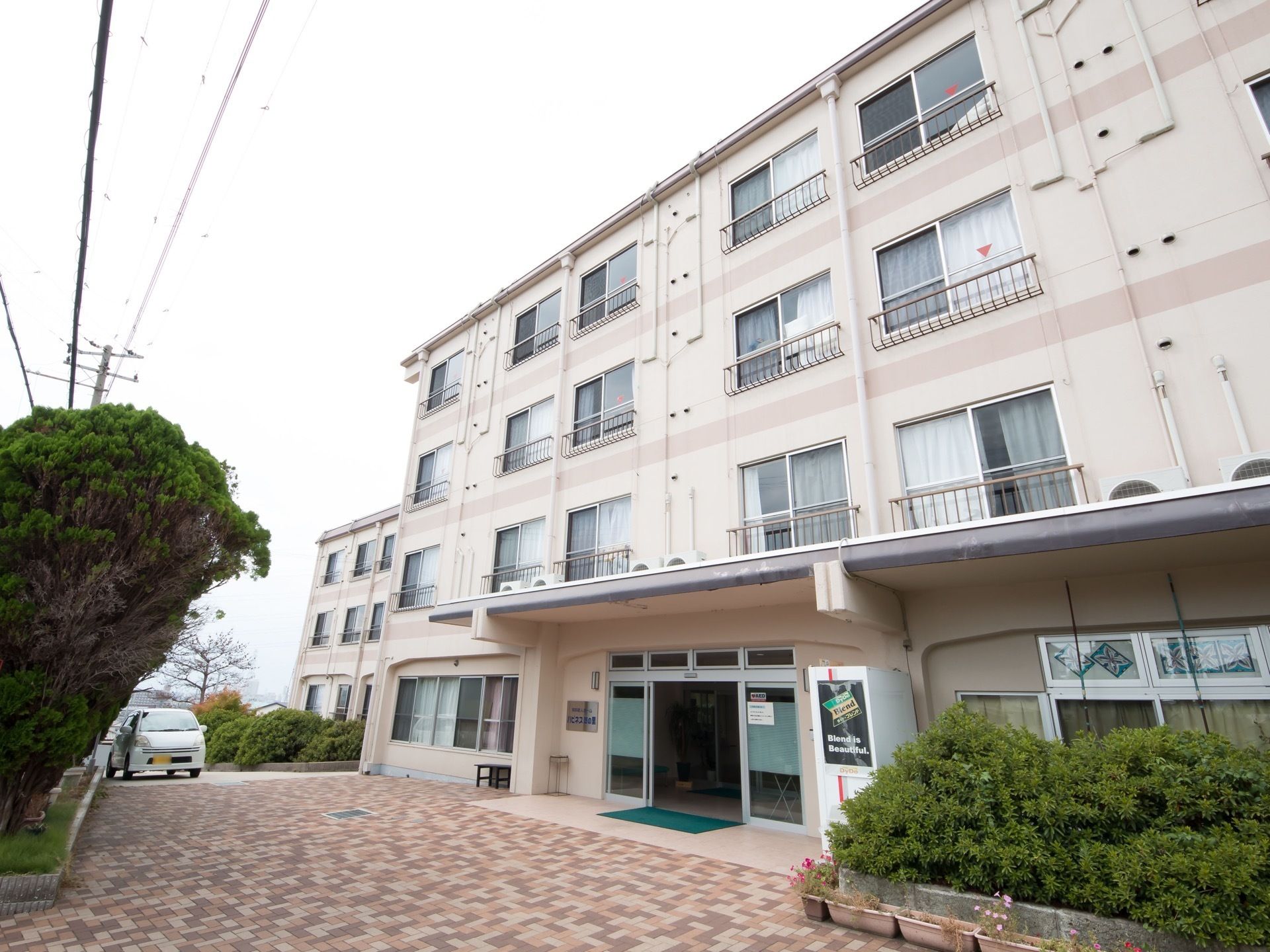 施設前の道は、レンガ模様でプランターが多数置いてある。建物は薄いベージュで、シンプルなデザインである。