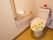 温水洗浄便座がついた個室のトイレ。花柄のトイレカバーと、小さな鉢植えが置かれている。壁にはL字型に手すりが設置されている。
