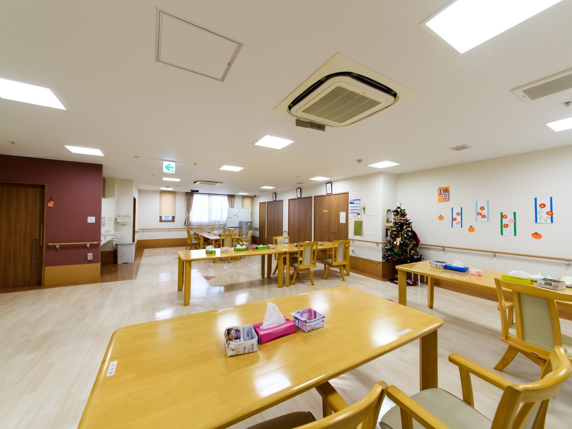 食卓のテーブルの上にはティッシュペーパーの箱や広告の紙で作ったごみ入れが置かれている。壁にはコスモスの花の作品が飾ってある。