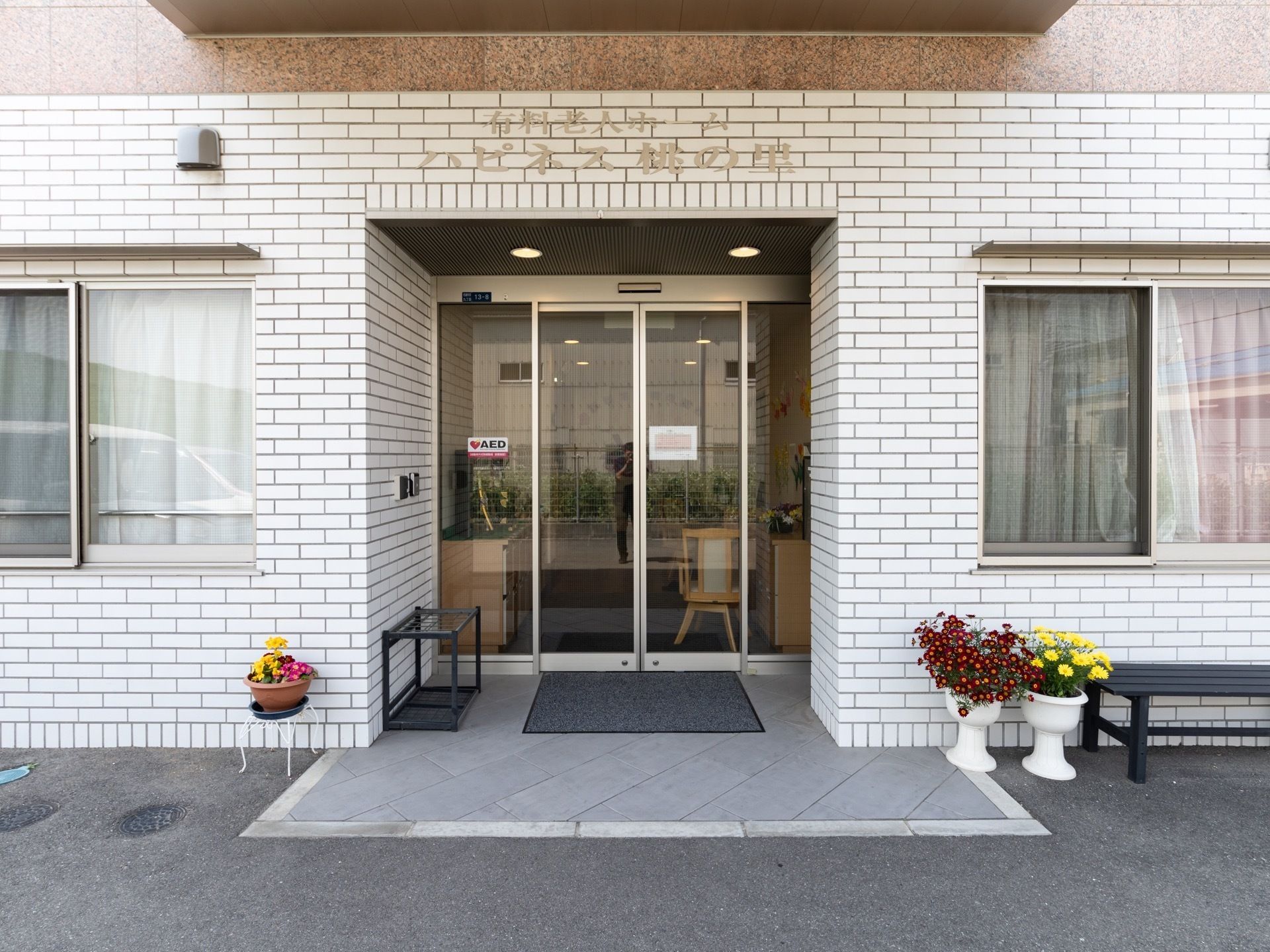 玄関前には両サイドに植木鉢が置かれている。共同利用の傘立てが置かれ、入口上には施設名の表示がされている。