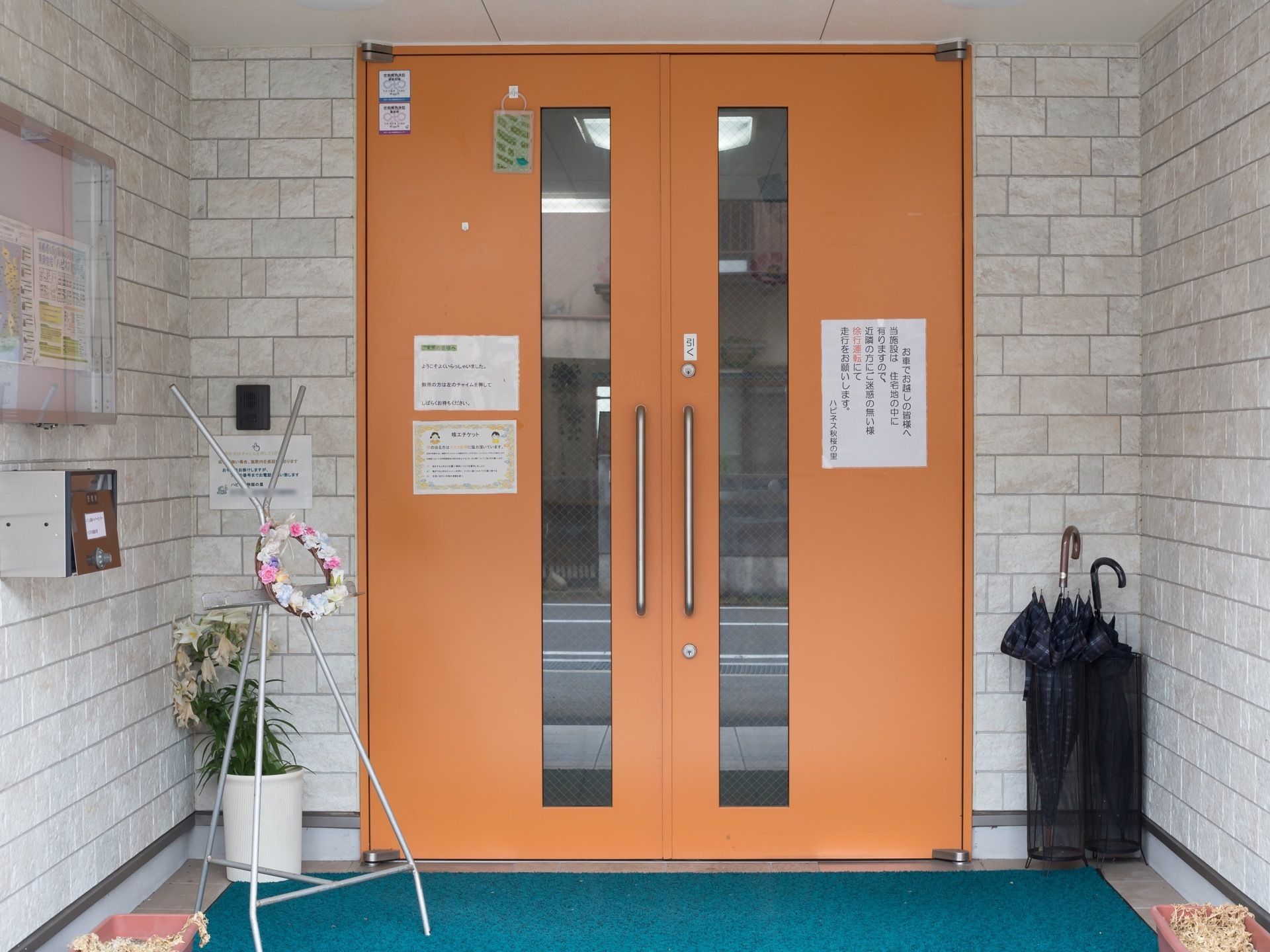 施設の入口の扉は明るい色合いをしており、両側が開閉するタイプの設計である。側面の壁はレンガ調に統一されており、壁にはインターホンがある。