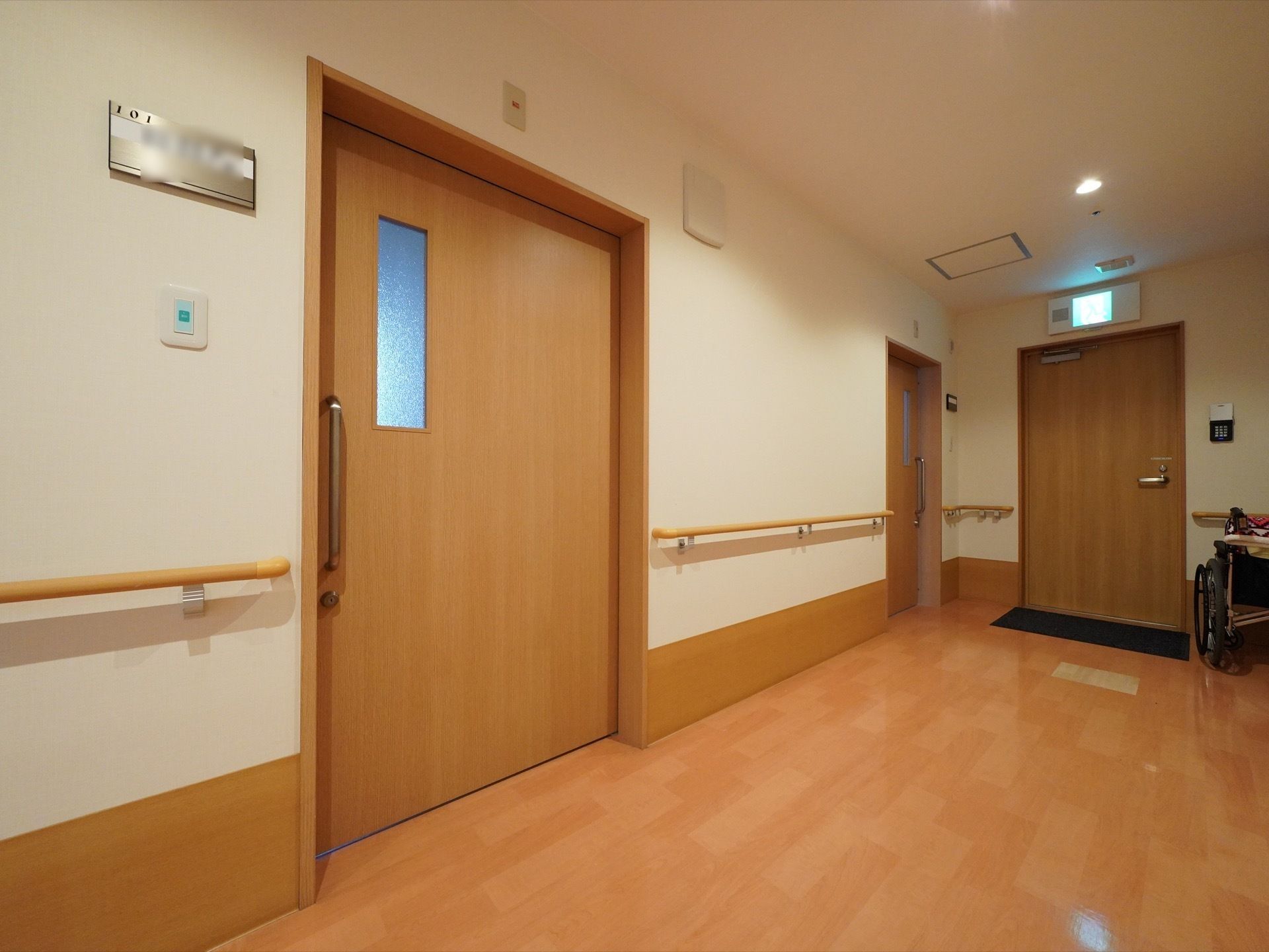 通路には明るい色調の木材を使っている。居室の扉は小窓付きの引き戸で、入り口の壁には名前用のプレートを設置している。