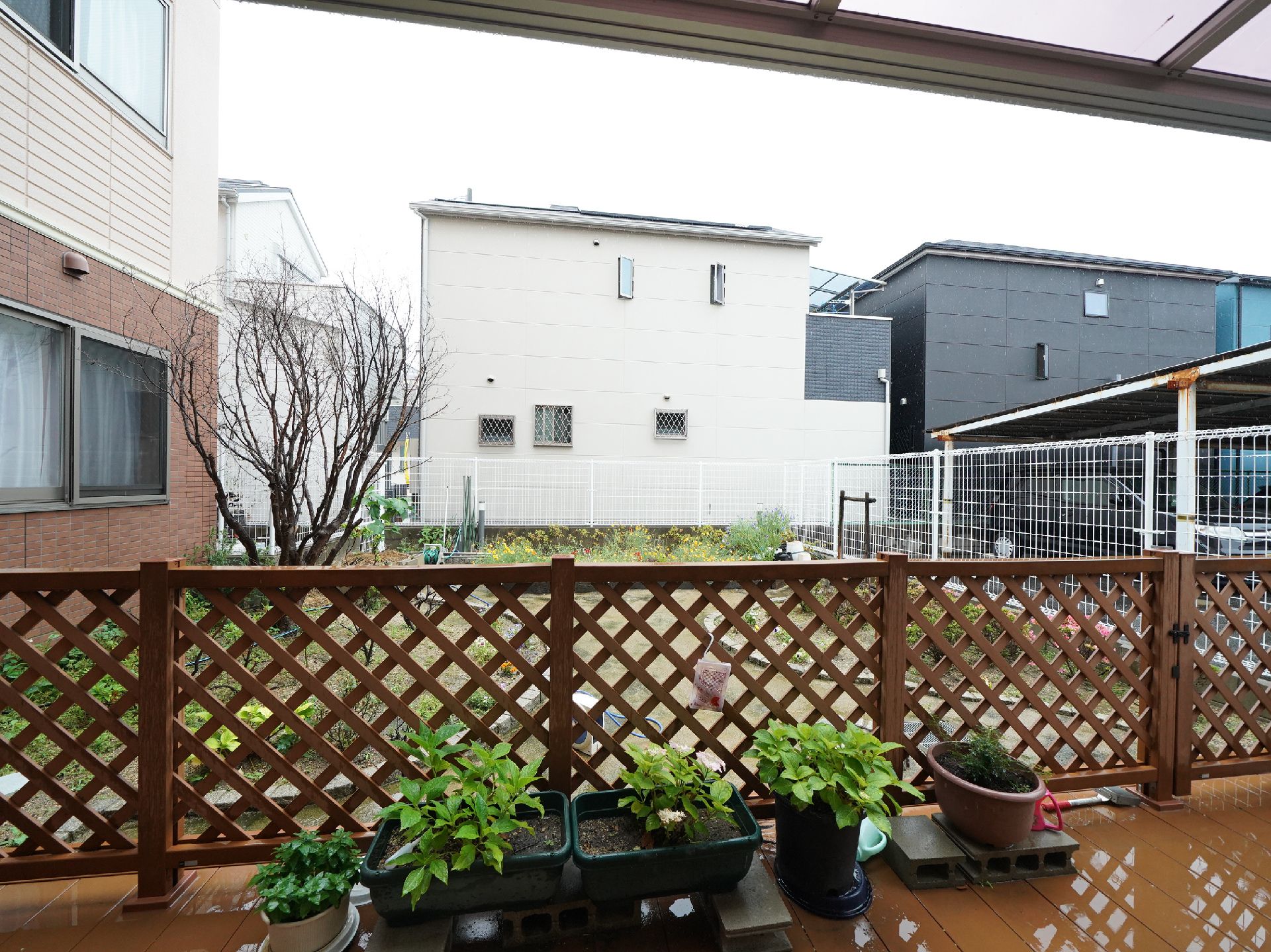 鉢植えがそばに置かれ、木材の柵の奥に中庭のあるテラス