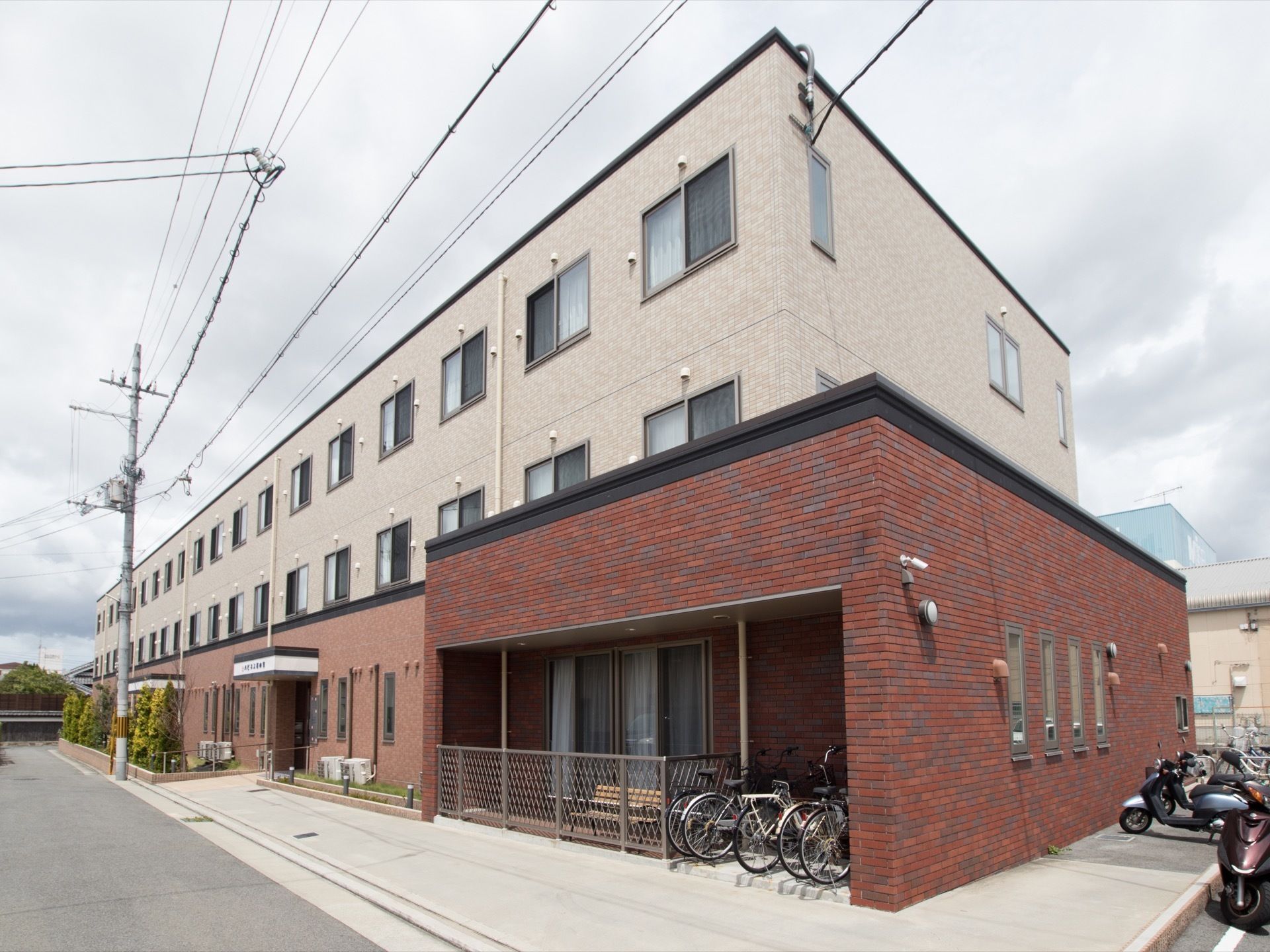 道路に面したところに立地する、3階建ての施設である。あたたかみのあるレンガ調の外壁が印象的。駐輪場もある。
