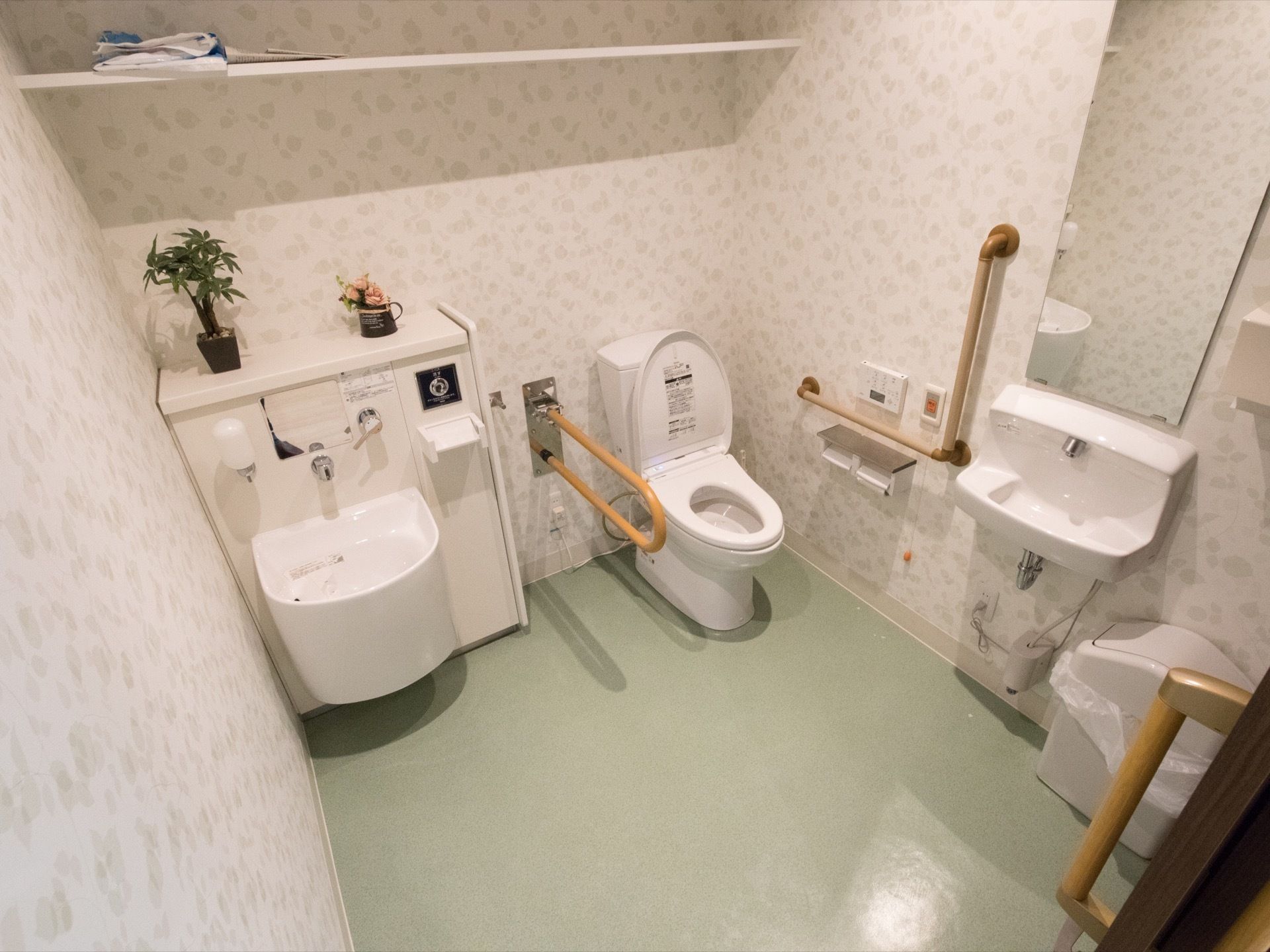 淡いグリーンの床にホワイト調の壁で施工された、オストメイト対応のトイレである。手洗い場も設置されている。