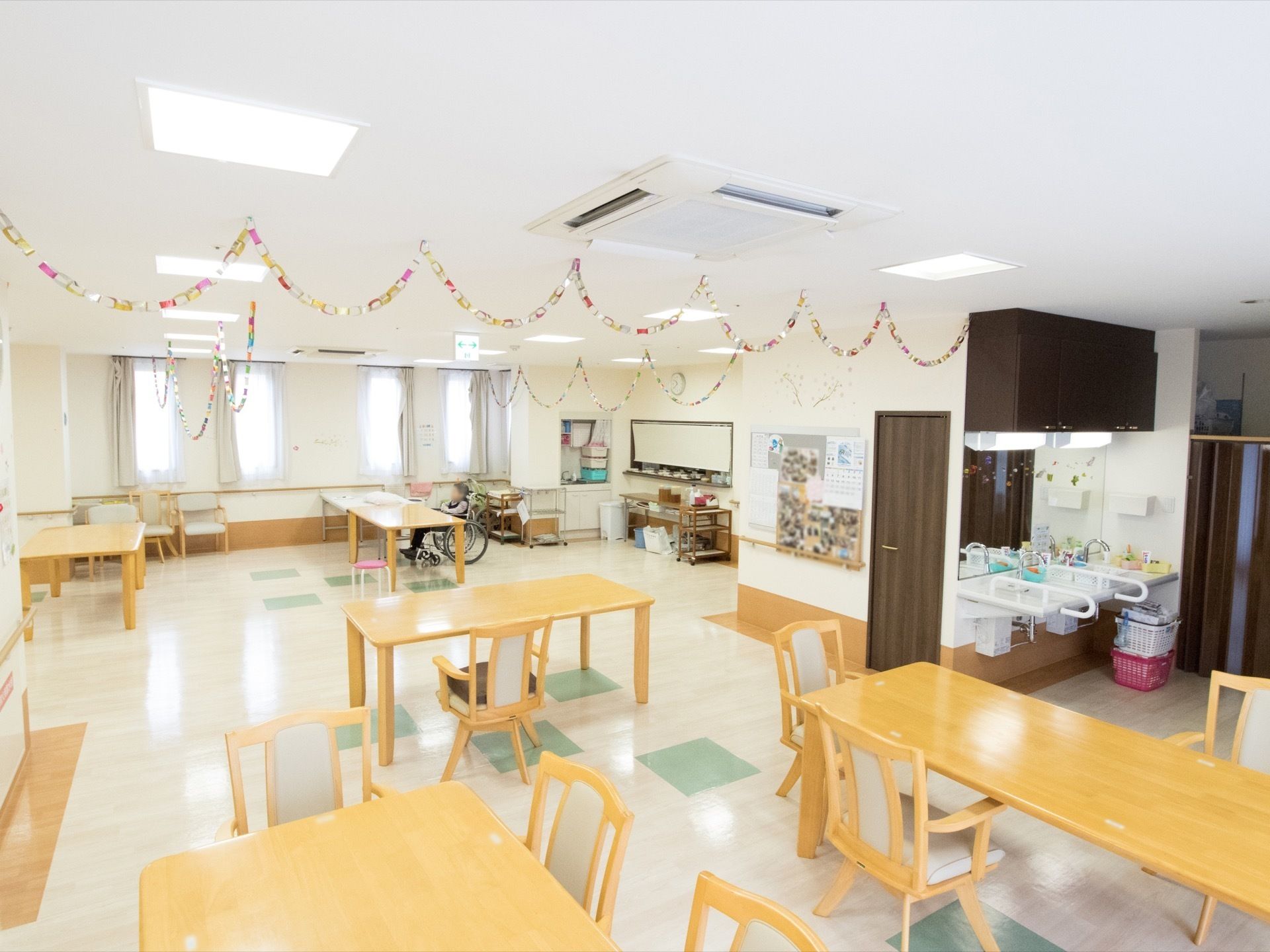 広々とした食堂で開放的である。木製のテーブルセットが配置されている。天井に空調機も備えつけられてある。