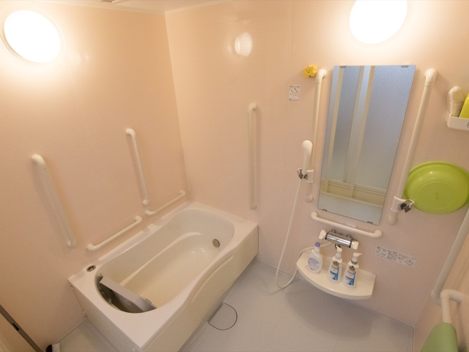 丸型の照明が備えつけられた、あたたかみのある浴室である。壁に縦型、横型の手すりが複数設けられている。