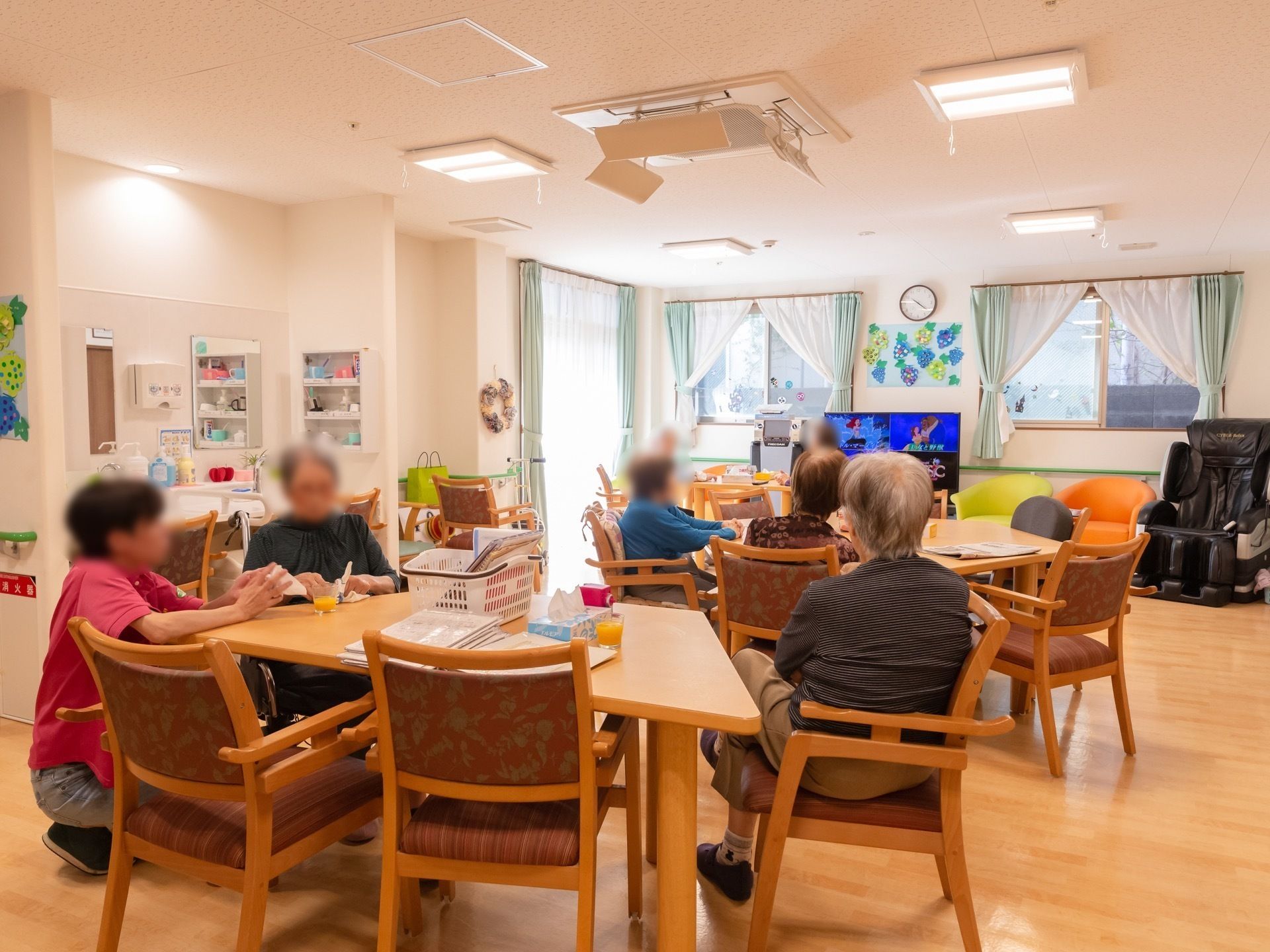 食堂の椅子に座り、テレビを見たり、折り紙を折ったり各々の活動をする入居者たち