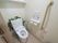 造花で彩られたトイレはきれいで清潔感ある作りとなっている。立ち上がり用の手すり、非常ベルも完備しており、安全安心の設備が充実。