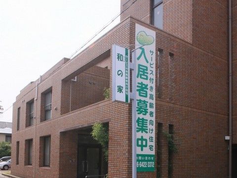 窓がいくつも付いているレンガ色の温かみのある建物である。入口の屋根の下には背の高い植物が置かれている。
