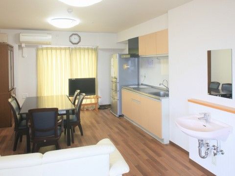 空間の中央にダイニングテーブルと椅子が配置されている。黄色いカーテンが引かれた窓があり、その横にはエアコンが設置してある。