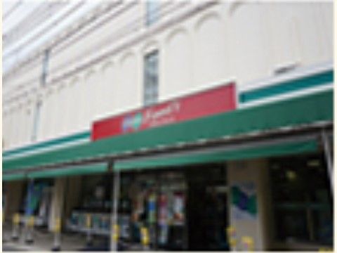 当施設の近くにあるスーパーマーケットの入口である。赤い看板が取り付けられた緑色のひさしの下には商品が並んでいる。