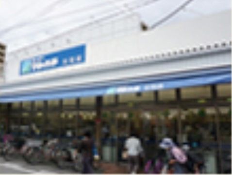 白い建物のスーパーマーケット。入口前にはたくさんの自転車が停められており、店内は客で賑わい活気がある。
