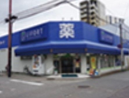 白色と青色の外壁のドラッグストア。入口の前には緑色のマットが敷かれていて、その横には自動販売機が置かれている。